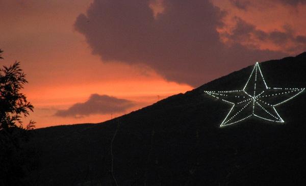 Star-shaped lights on a hill at sunset with an orange sky.