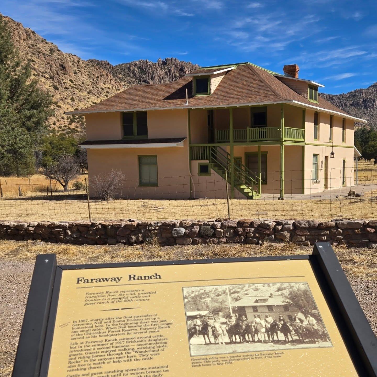 Faraway ranch under a clear blue sky; informational sign in foreground.
