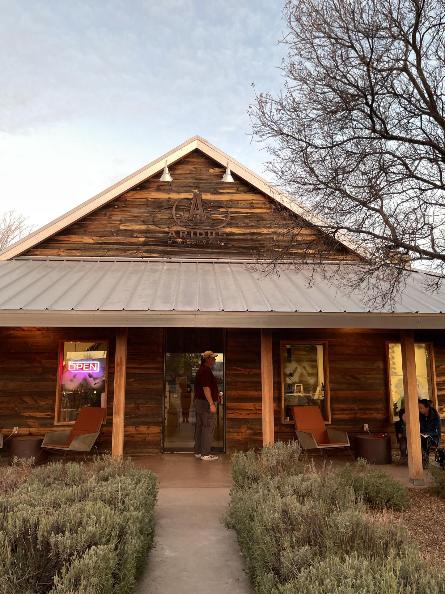 Rustic wooden building with a tin roof, chairs on the porch, and leafless tree nearby.