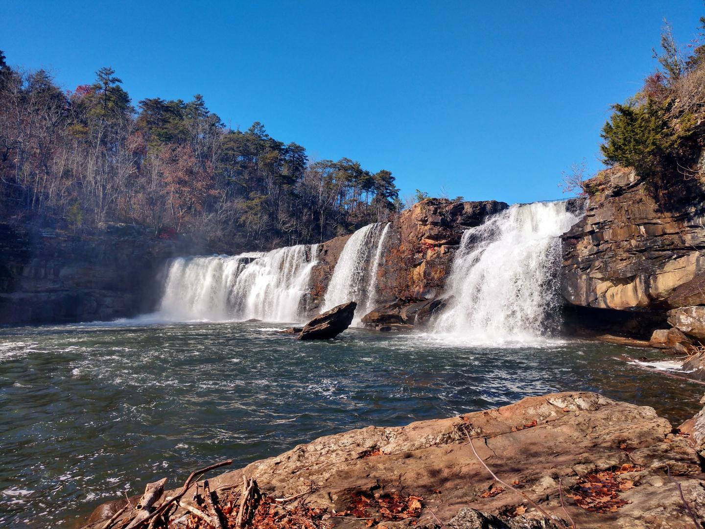 Waterfall cascading over rocky cliffs under a clear blue sky.