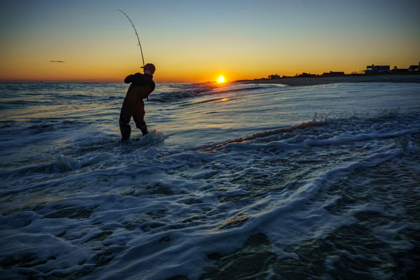 Fisherman casting line into ocean at sunset.