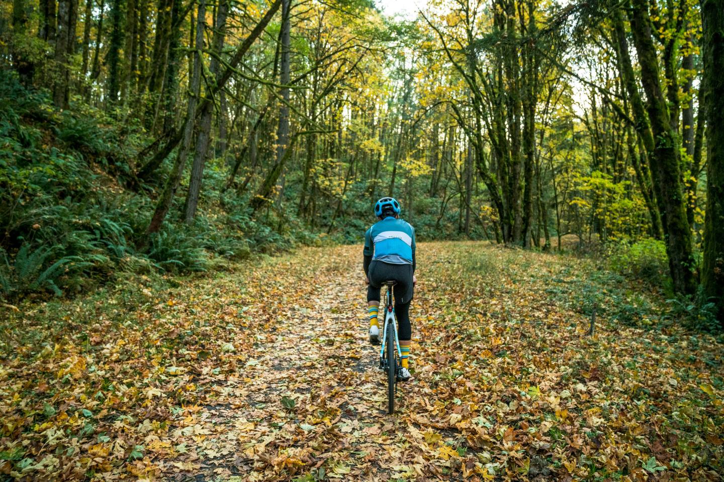 Cyclist riding through a forest path covered in autumn leaves.