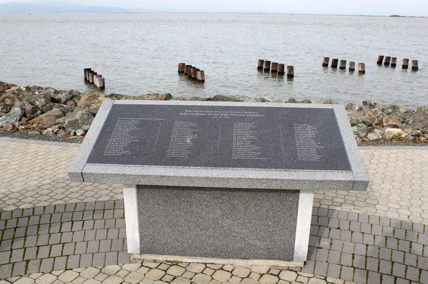 Stone memorial plaque by the seaside, on a paved pathway.