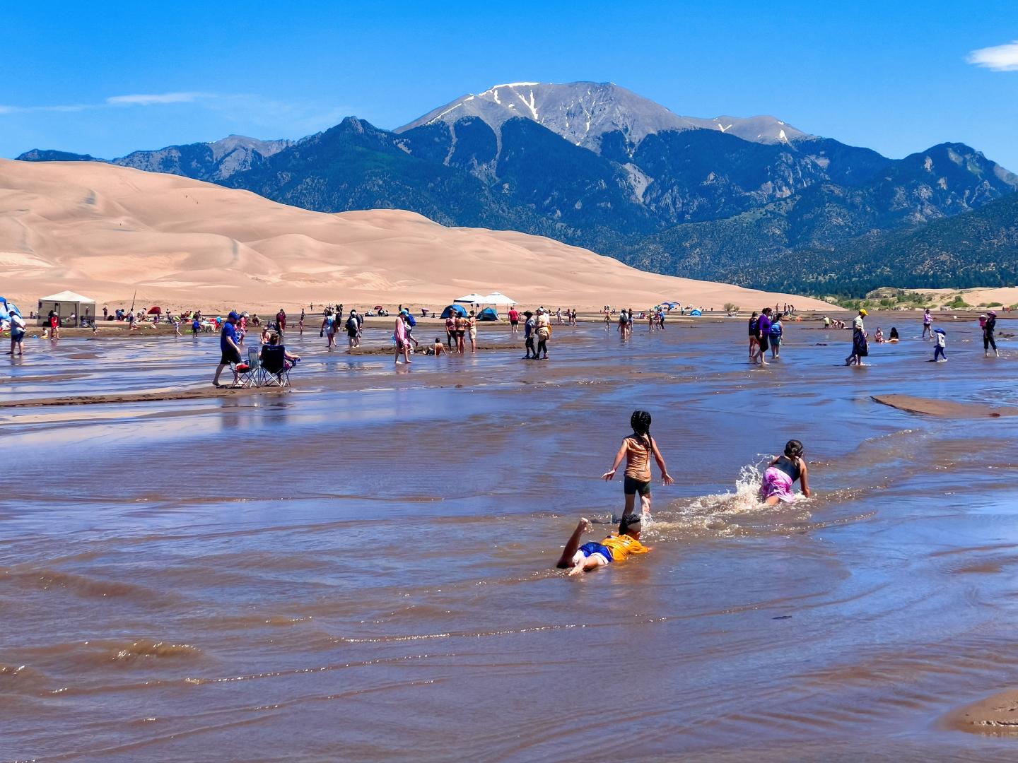 People enjoying Medano Creek with mountains in the background.