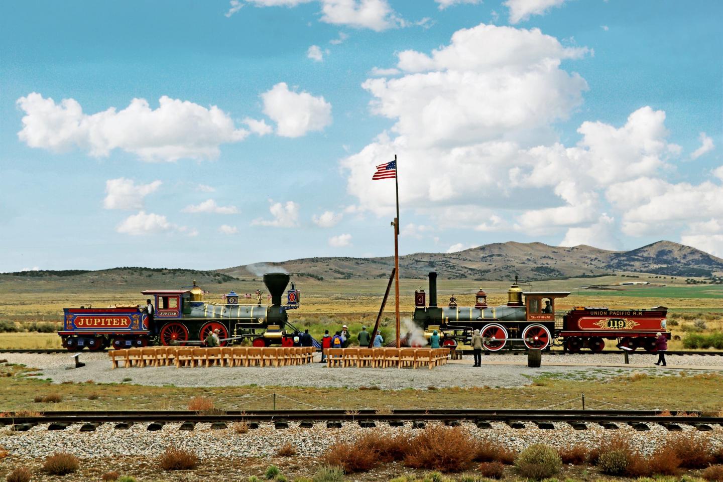 Two vintage trains facing each other outdoors with a U.S. flag in the background.