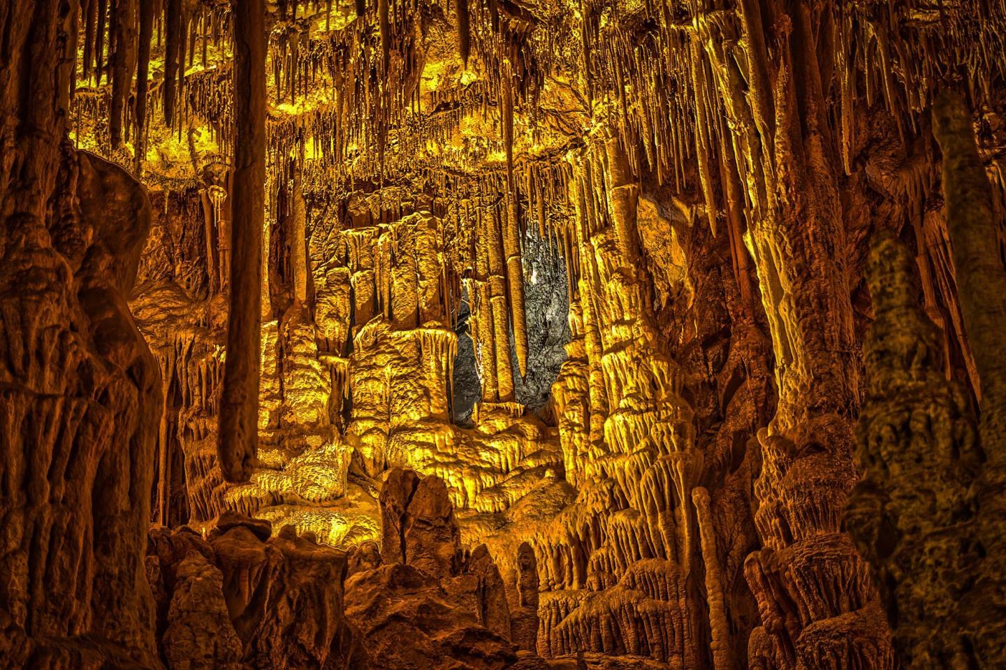 Glowing cave interior with stalactites and stalagmites in warm golden light.
