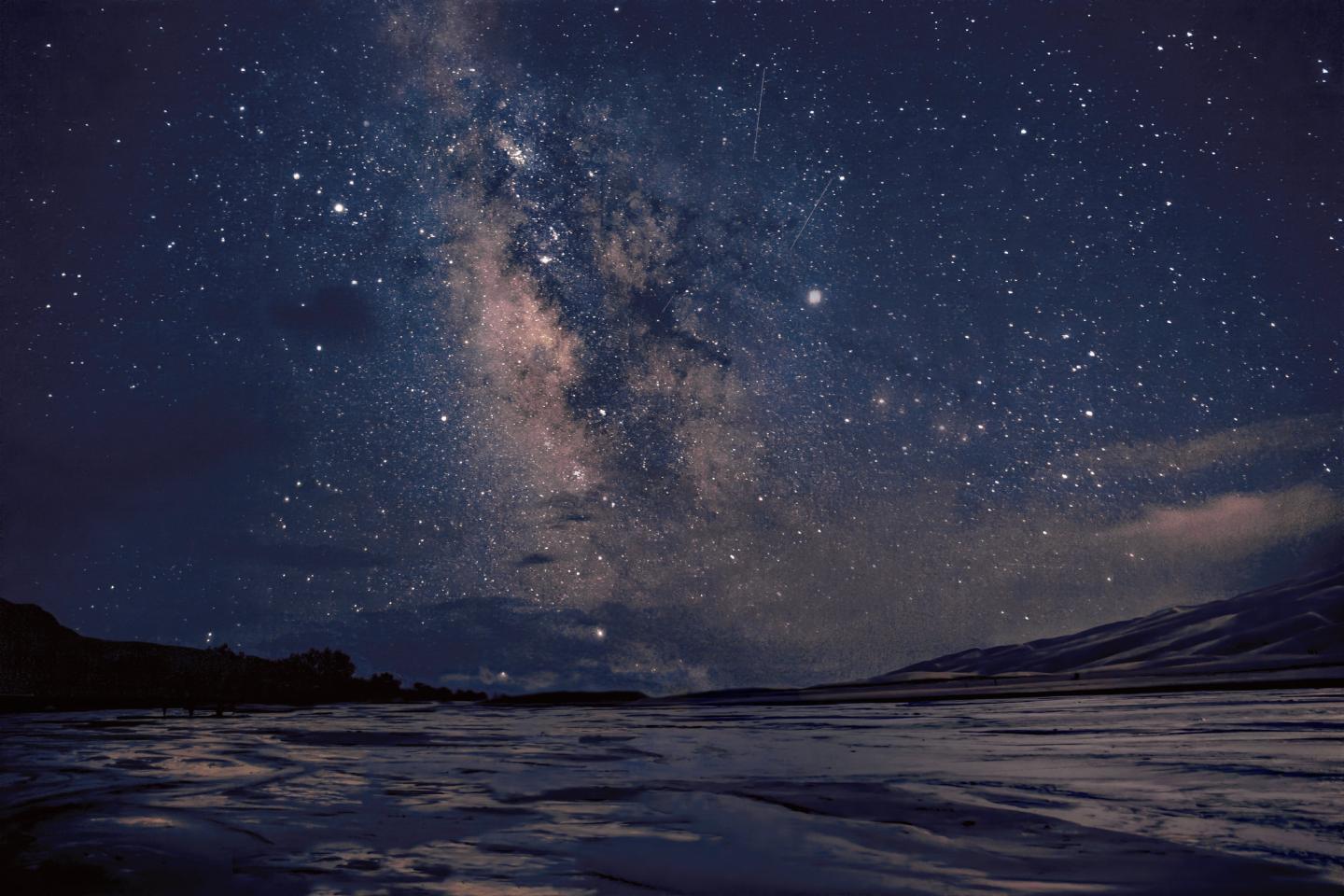 Starry night sky over a calm lake with distant mountains at Great Sand Dunes.