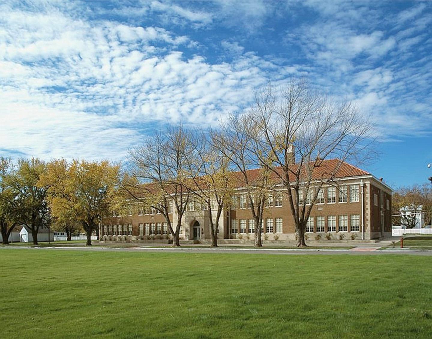 School with red roof, surrounded by trees, under a blue sky.