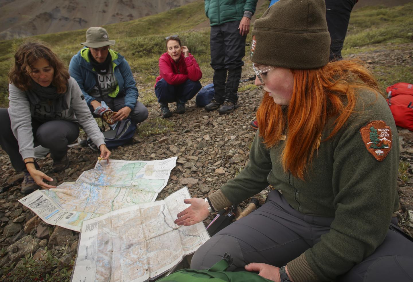 Park ranger and group study a map outdoors on rocky ground.
