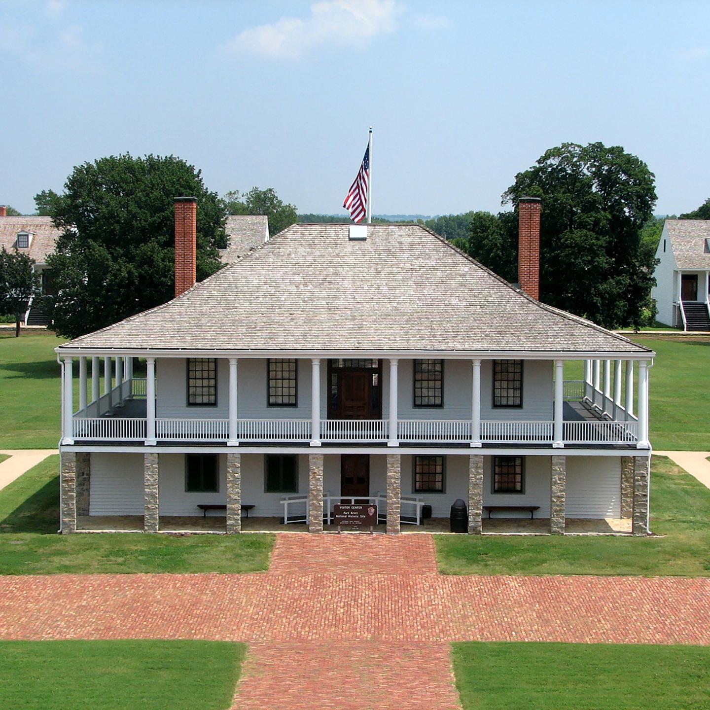 Fort Scott hospital building with stone columns and a U.S. flag, surrounded by lawn.