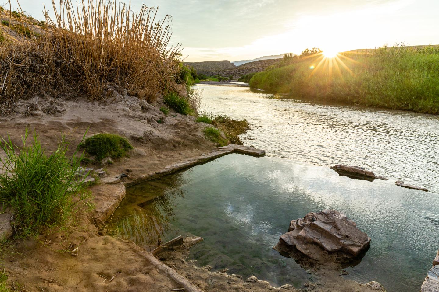 Big Bend hot springs at sunset with grassy banks and a rocky shore.