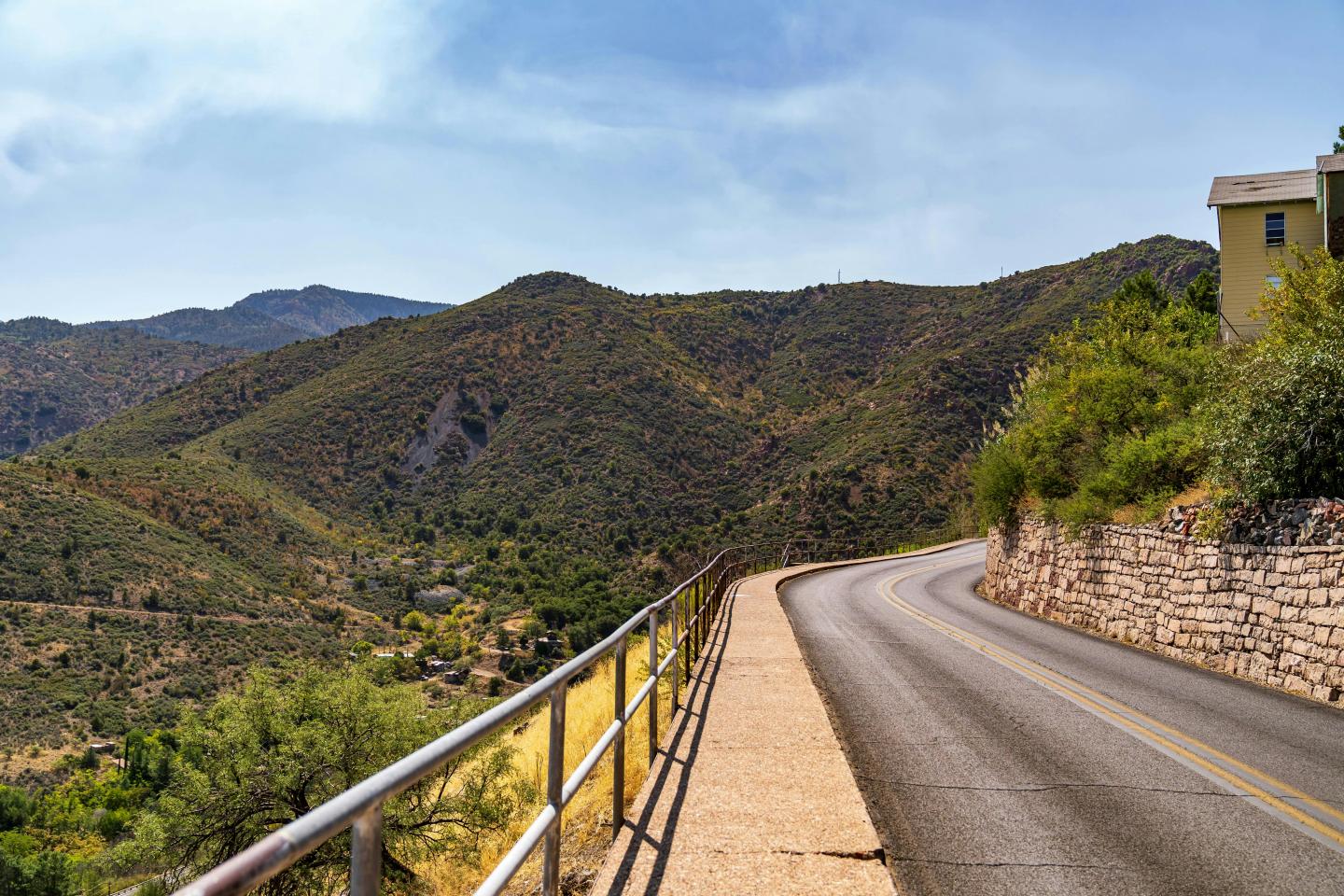 Curving road to Jerome alongside green hills under a clear blue sky.