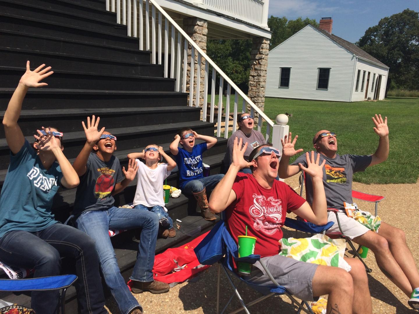 Junior rangers outside excitedly looking up, wearing solar eclipse glasses.