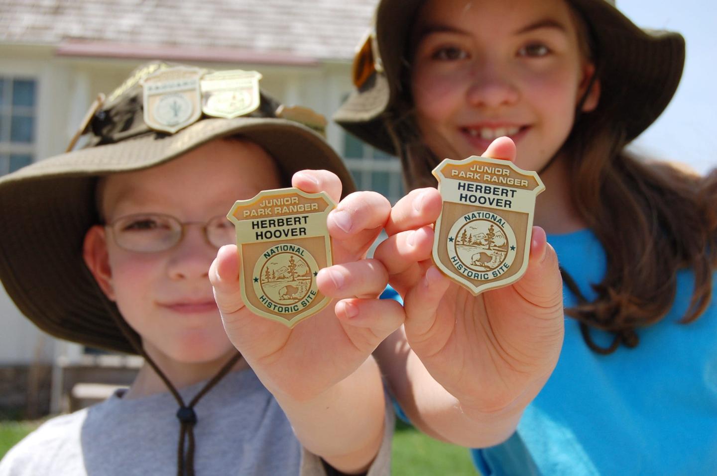 Children wearing hats proudly hold up badges outdoors.