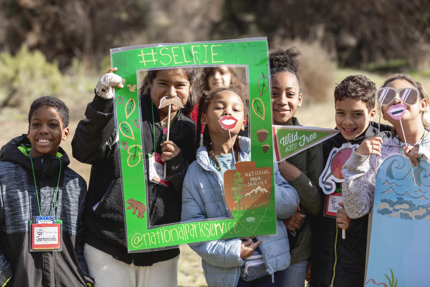 Group of smiling kids posing with a selfie frame outdoors.