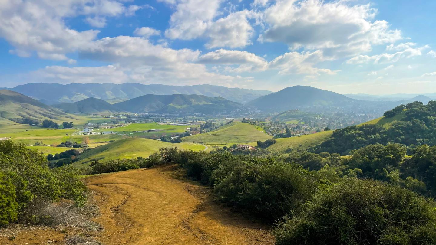 A dirt path leading through green rolling hills under a partly cloudy sky.