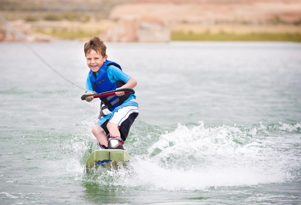 Child wakeboarding on a lake, smiling.