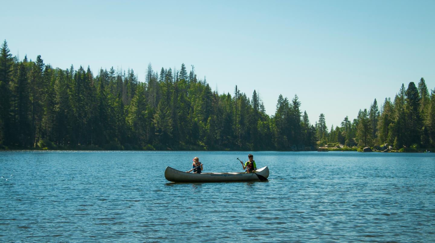 Canoe on a serene lake with tree-lined shore.