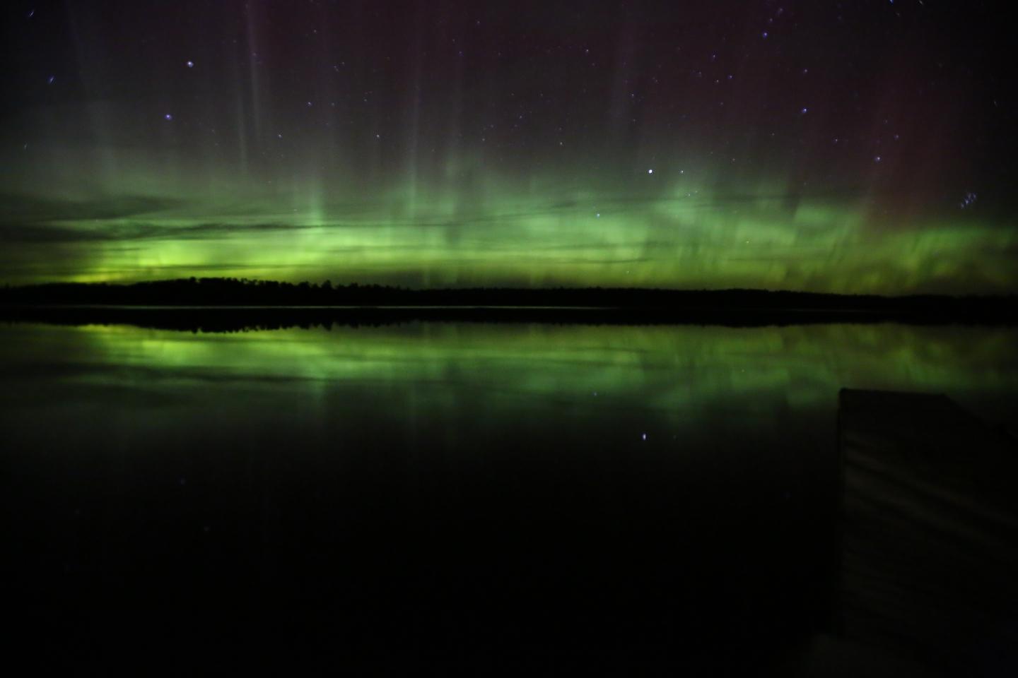 Northern lights reflecting on a calm lake under a starry sky.
