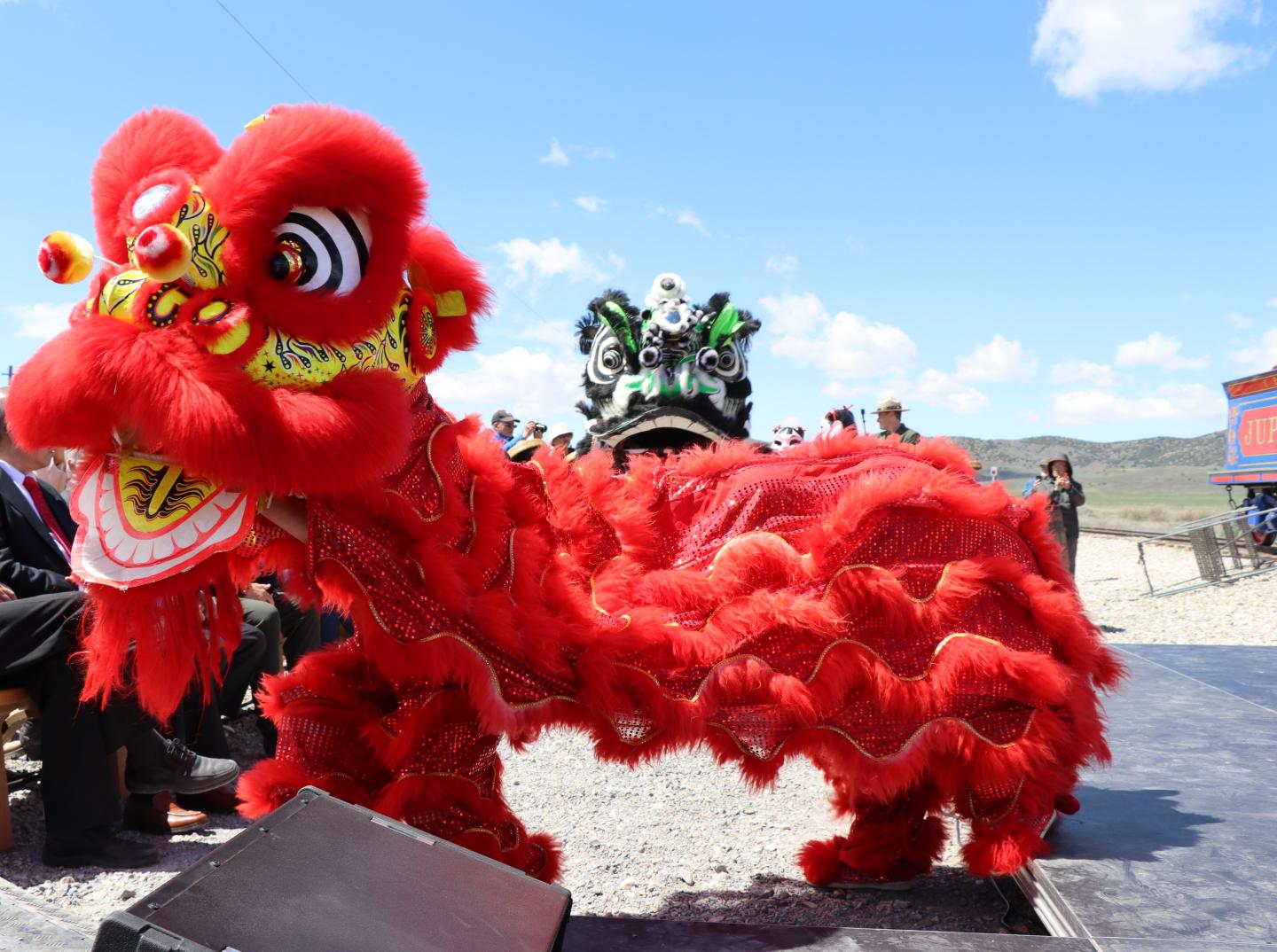 Red lion dance costume with greenery background, performed outdoors.
