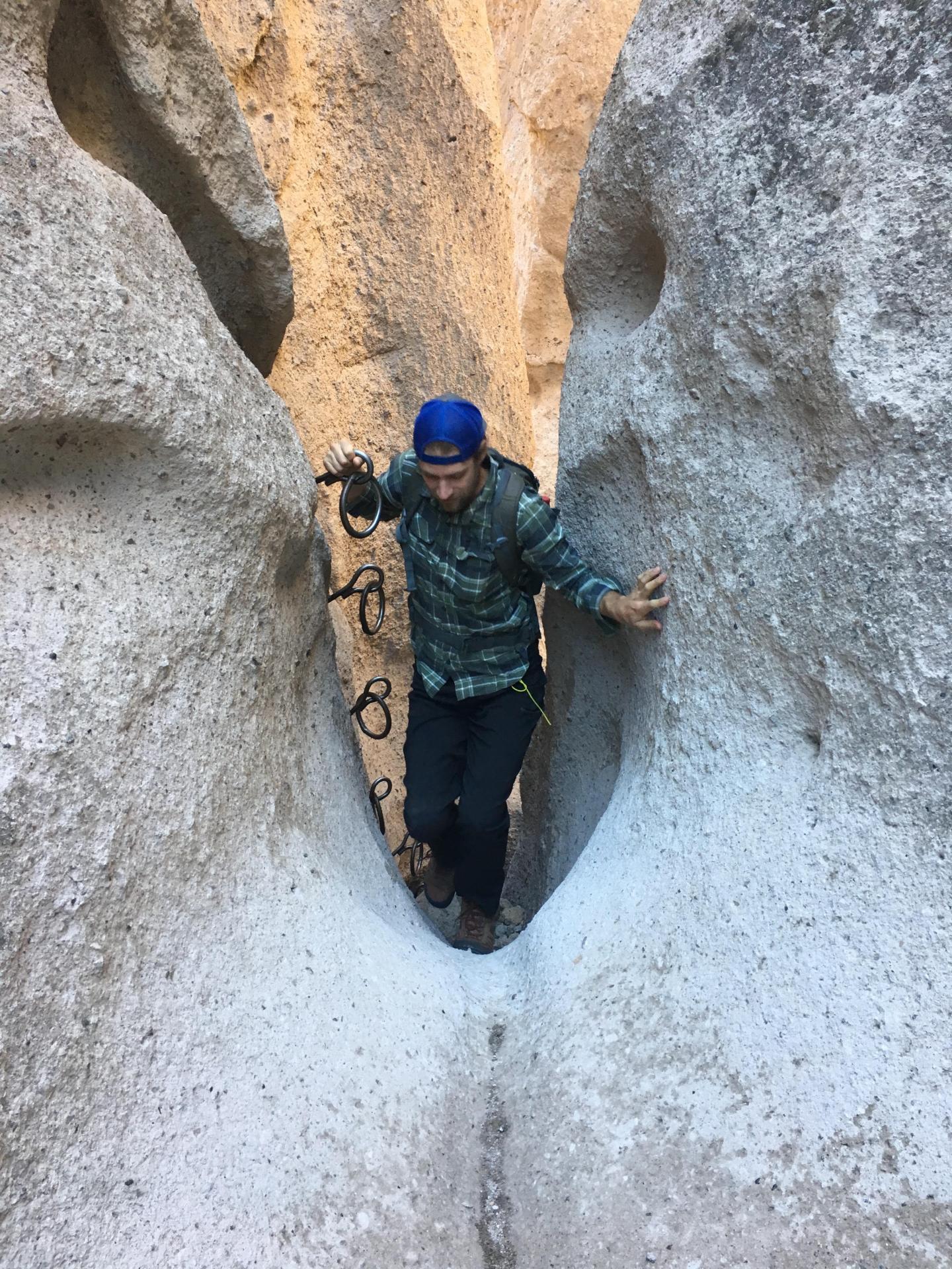 Climber in a narrow rock passage wearing a blue cap and green jacket.
