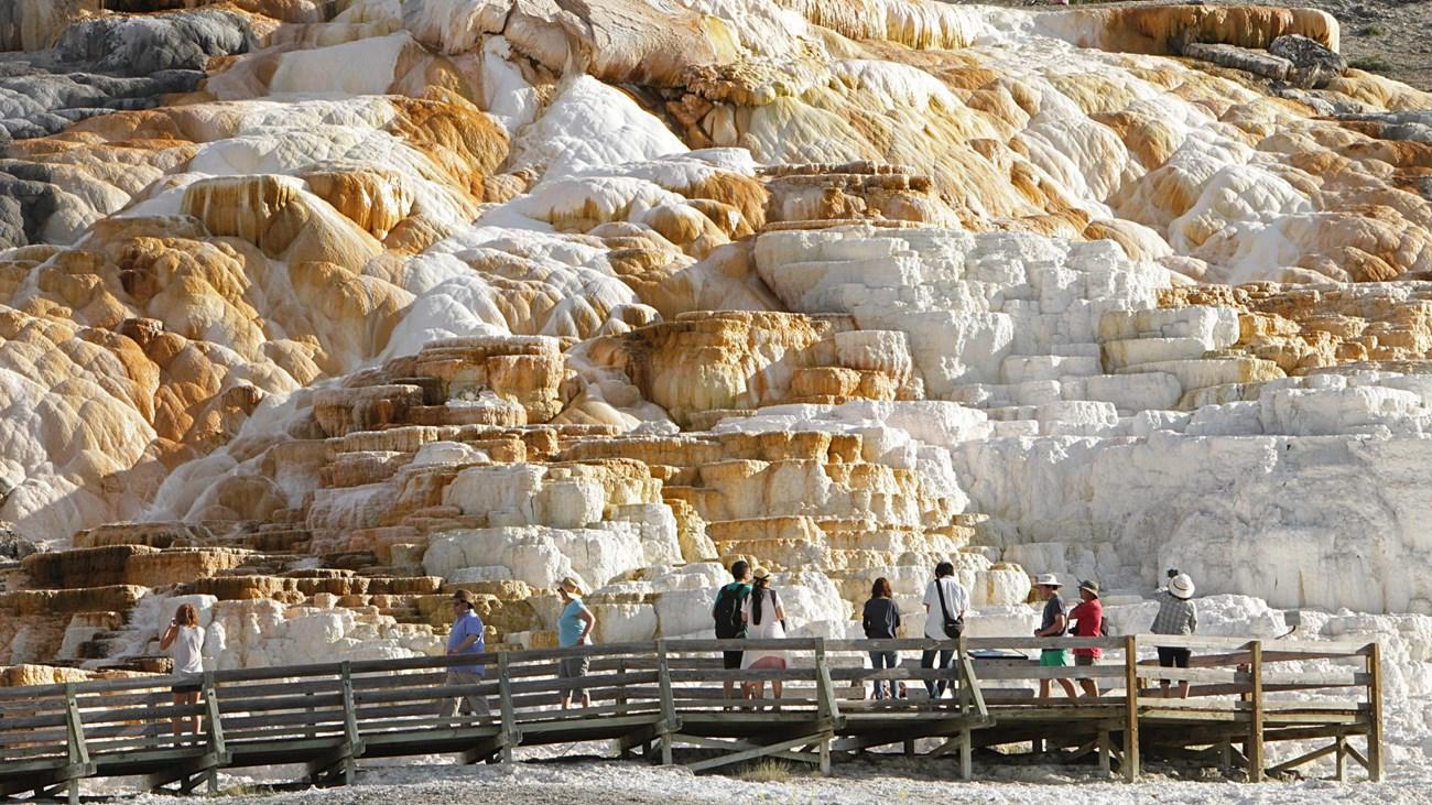 People walk on a boardwalk in front of a large, colorful rock formation.