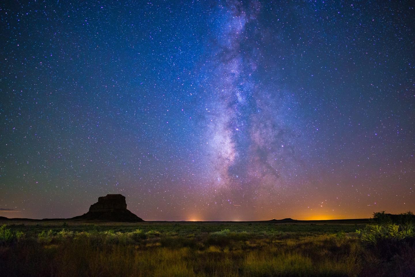 Starry night sky with Milky Way over a dark silhouette of a landscape.