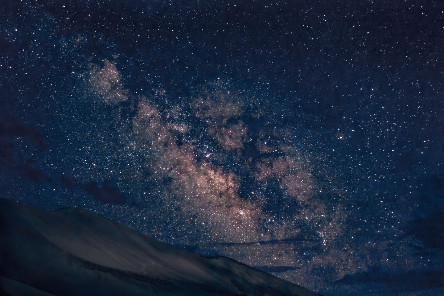 Starry night sky with Milky Way over silhouette of dark mountains.