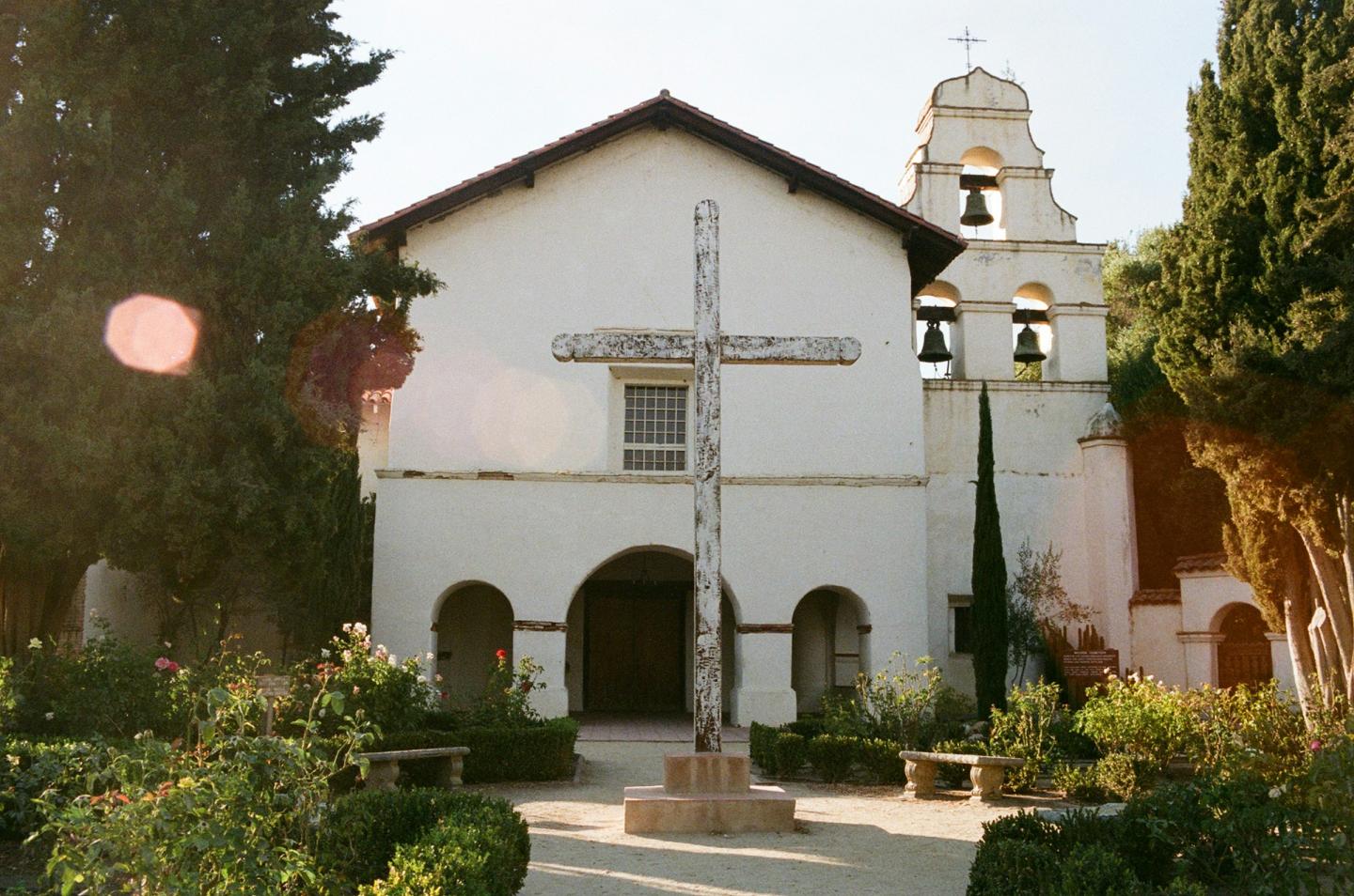 Mission San Juan Bautista with bell tower, garden, and central cross.