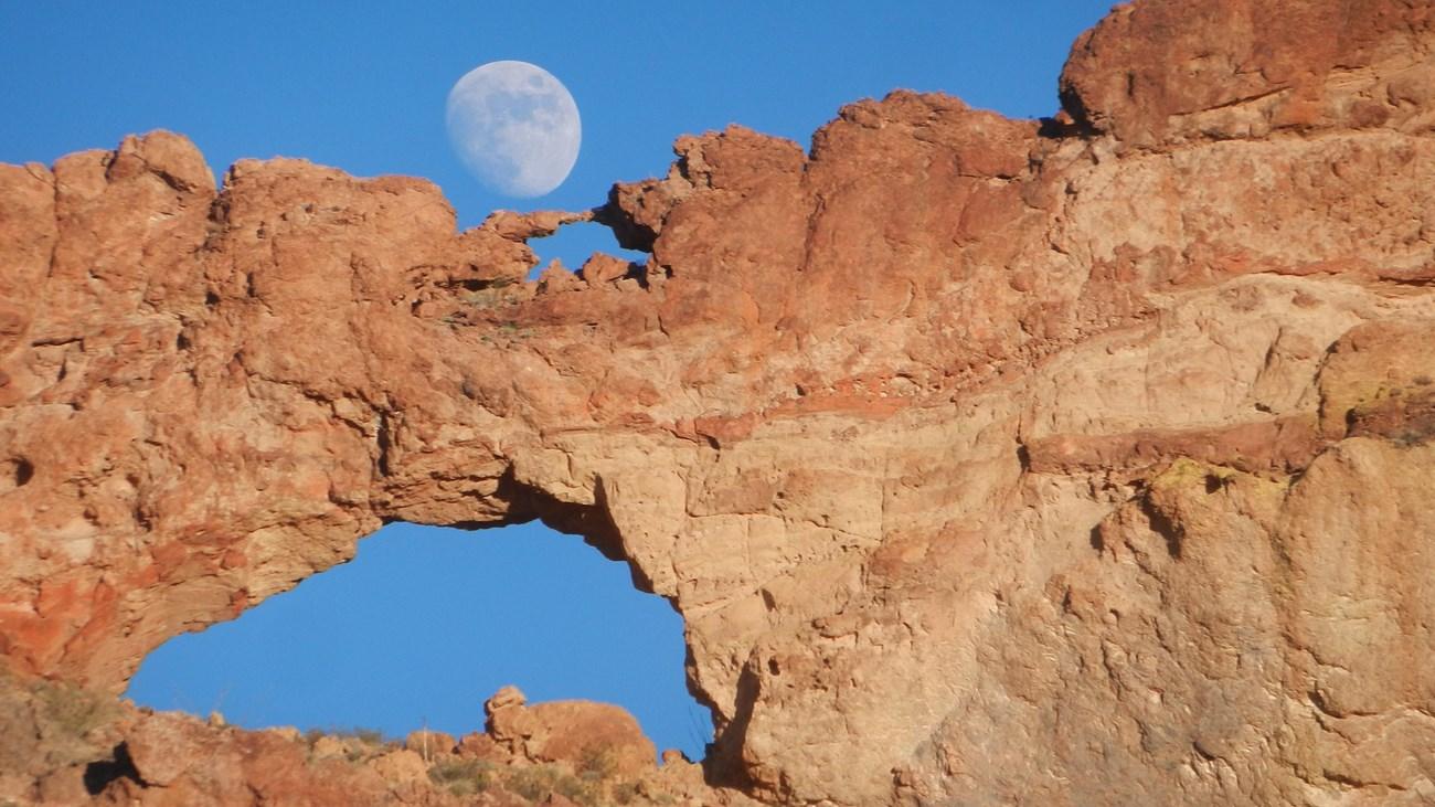 Rock arch against a blue sky with a visible moon.