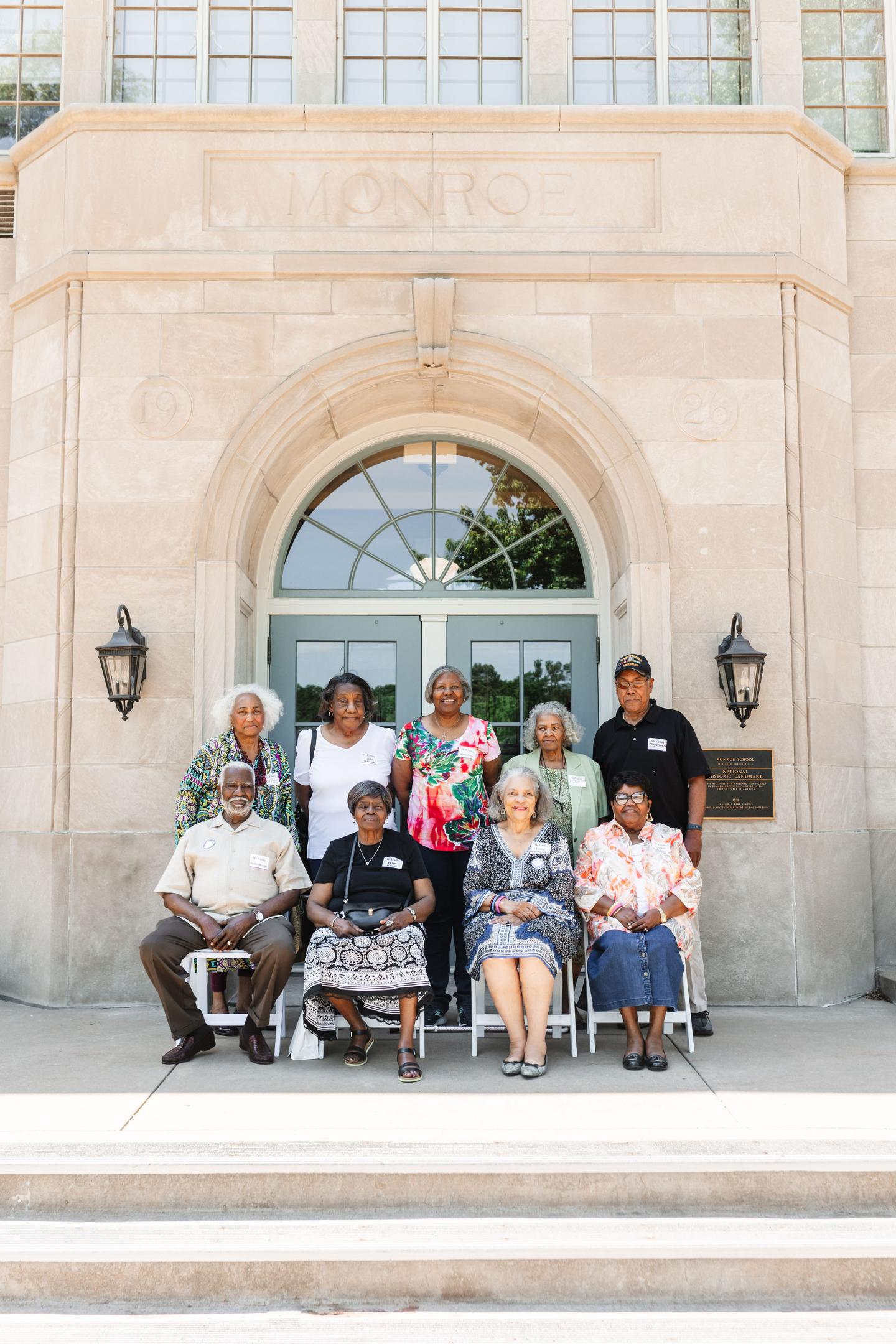 A group of people sitting and standing in front of a historic building at Brown v. Board of Education National Historical Park