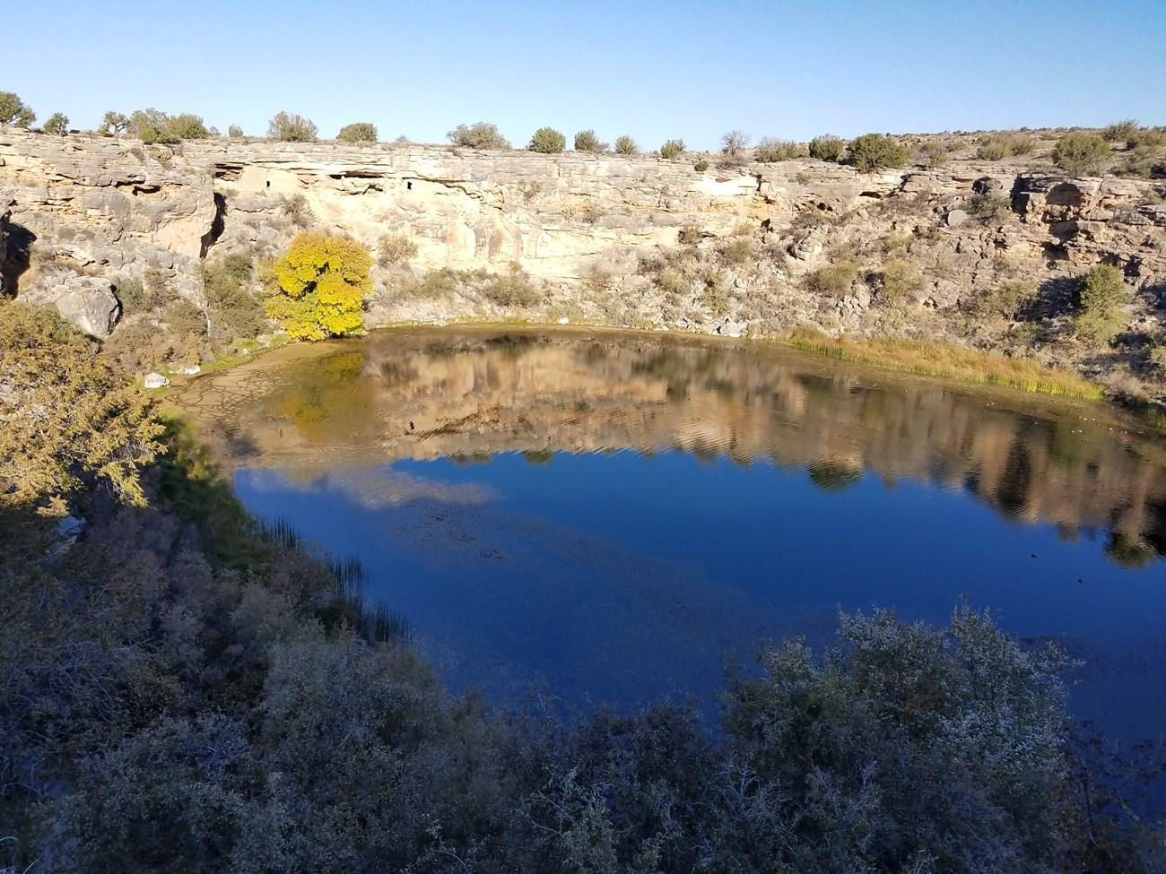 Montezuma well surrounded by cliffs and sparse vegetation under a clear blue sky.