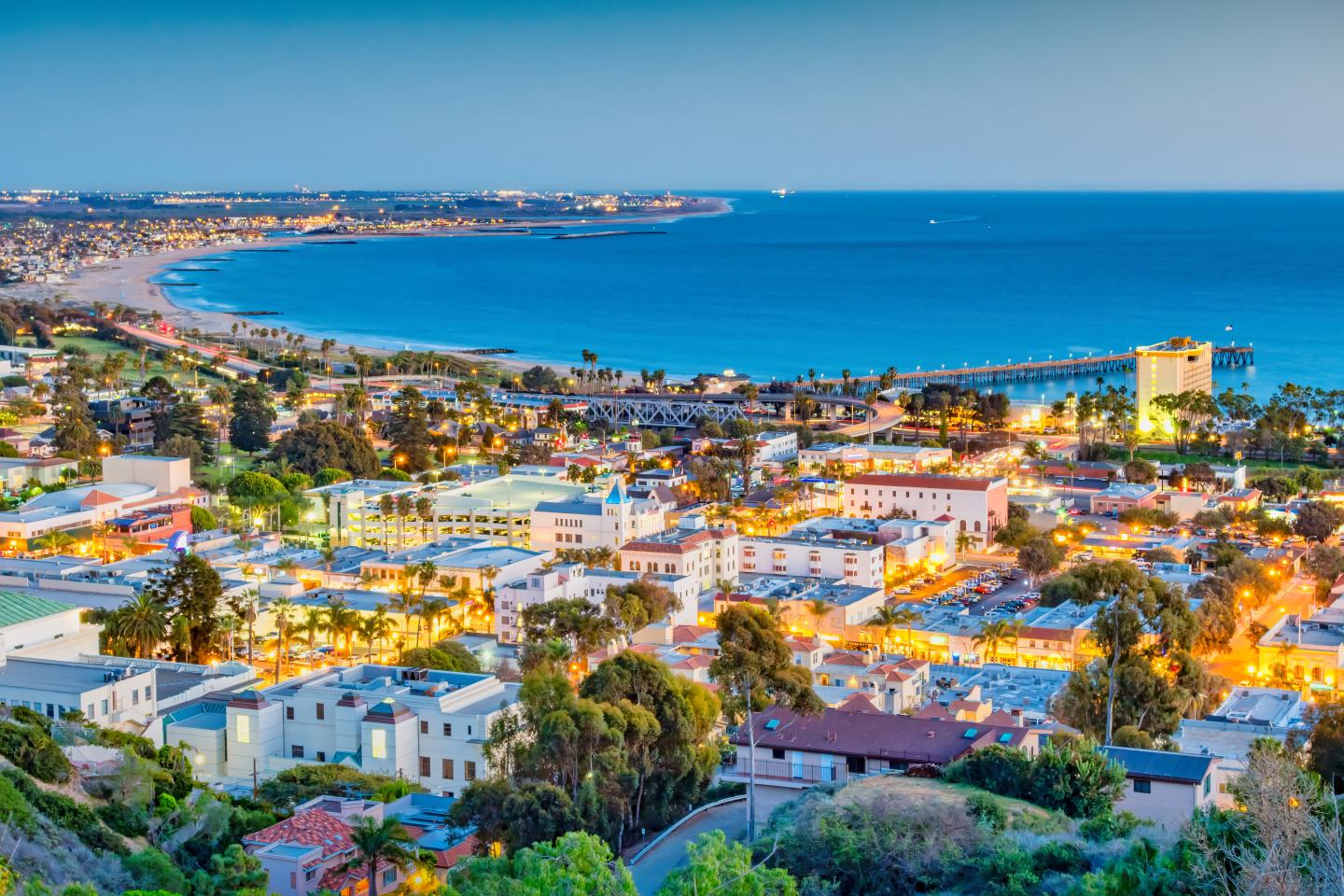 Coastal Ventura cityscape at twilight, vibrant lights, ocean in the background.