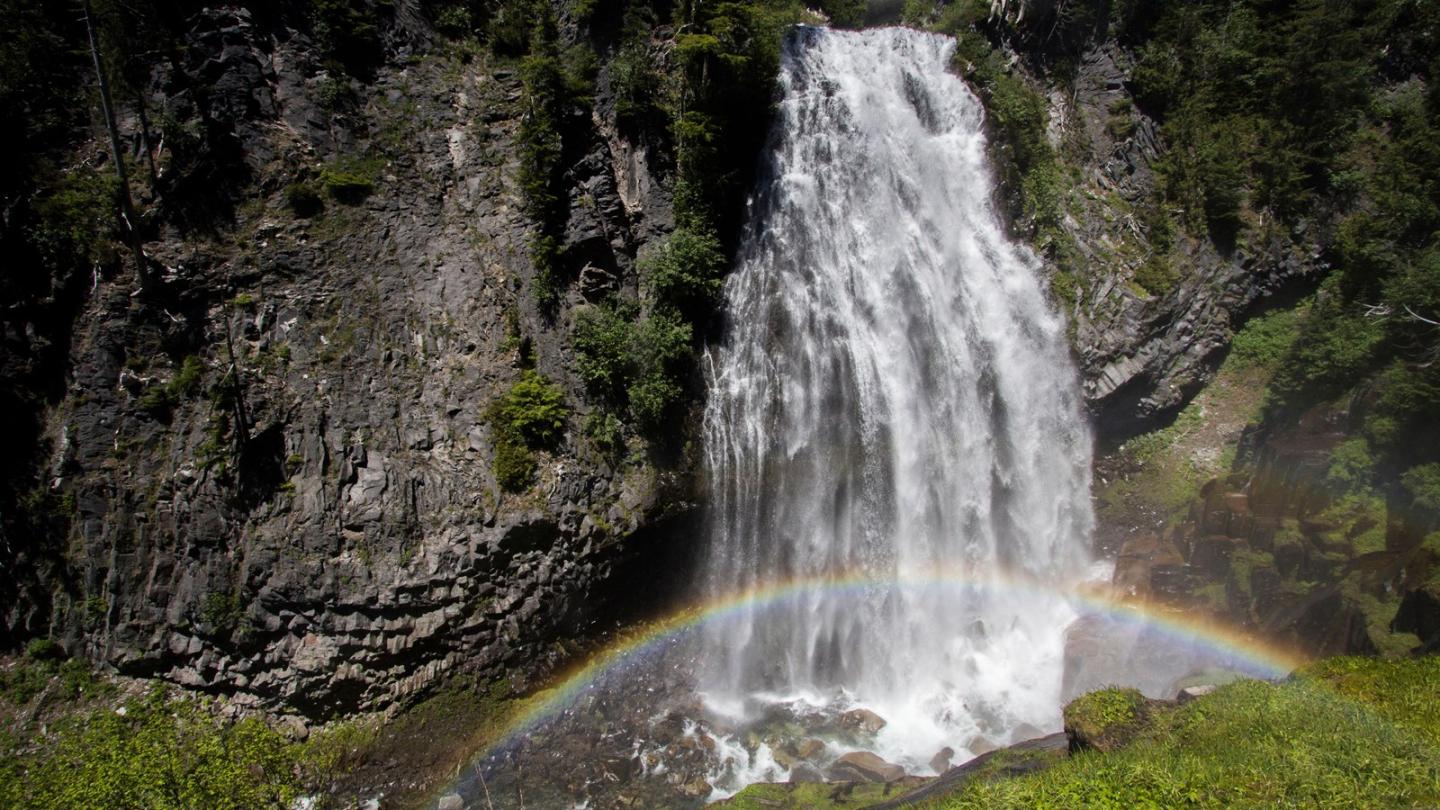 Narada Falls cascading down rocks with a rainbow in sunlight.