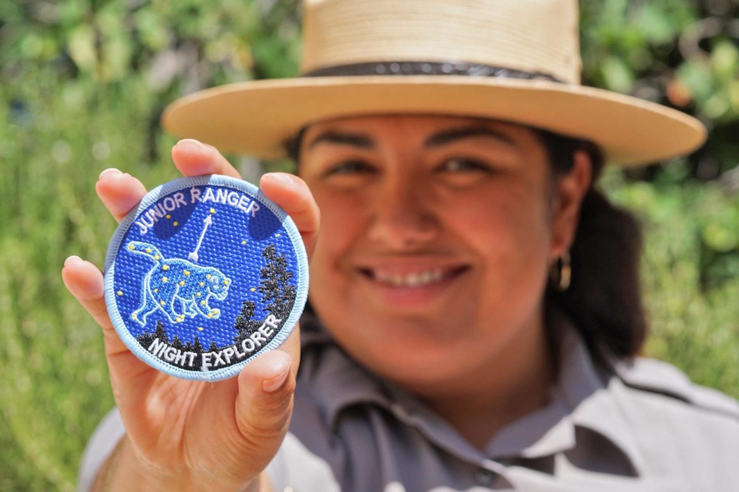 Smiling person holding a blue circular badge with a constellation design.