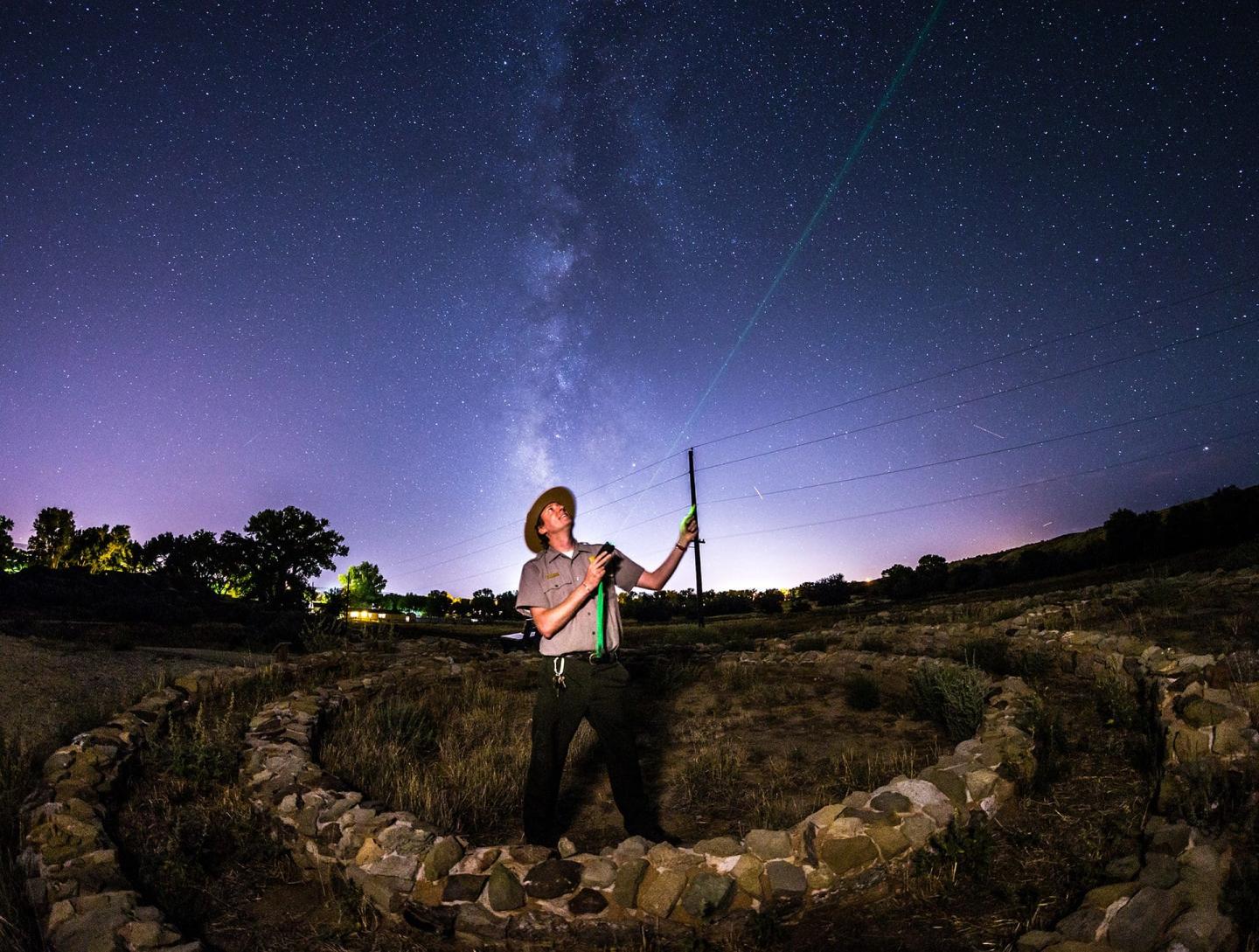 Person pointing a laser at the starry sky in a field at night.