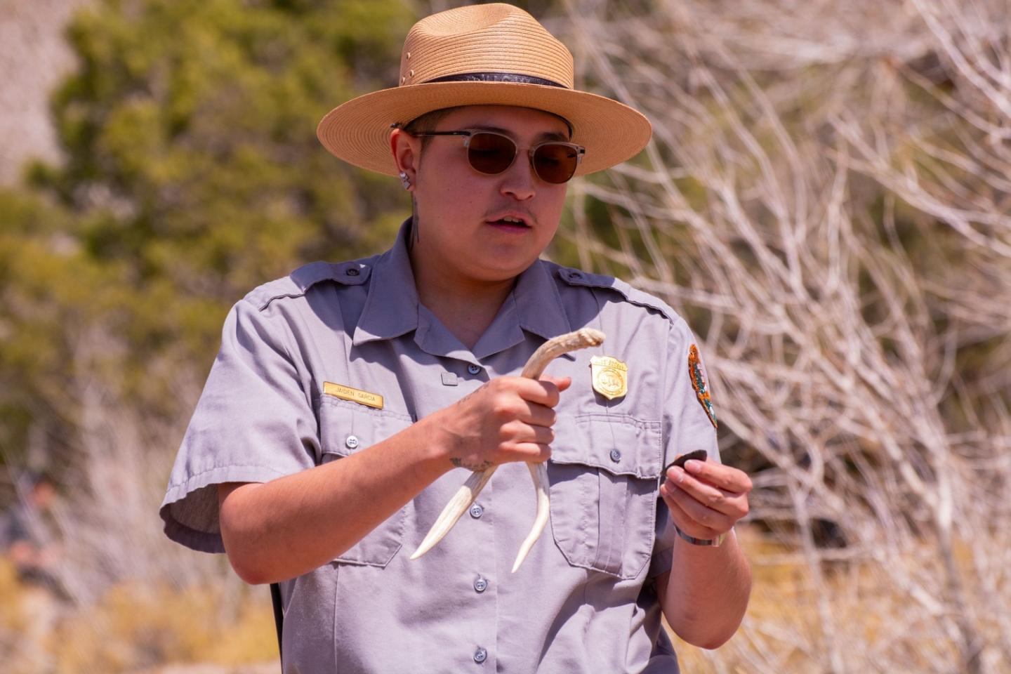 Park ranger with hat holding antlers outdoors.