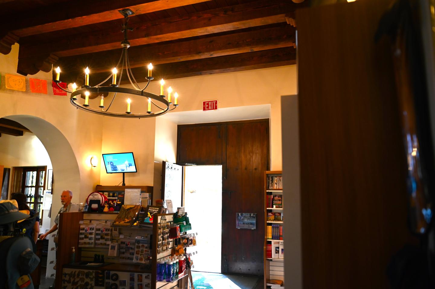 Dimly lit room with a chandelier, wooden beams, and various items on display.