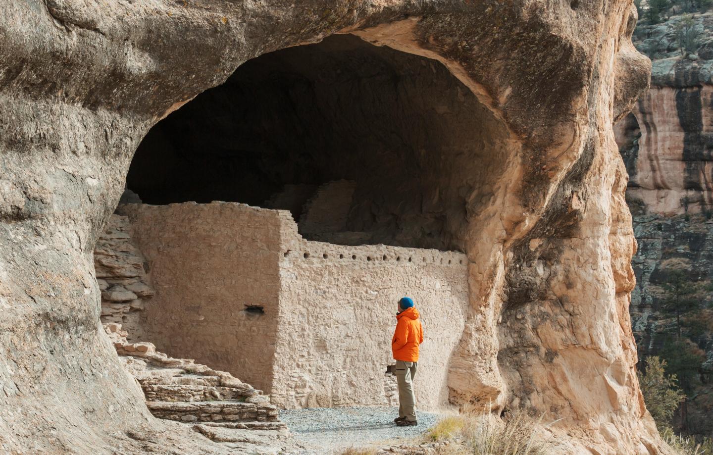 Cliff dwelling with a person in an orange jacket standing nearby.