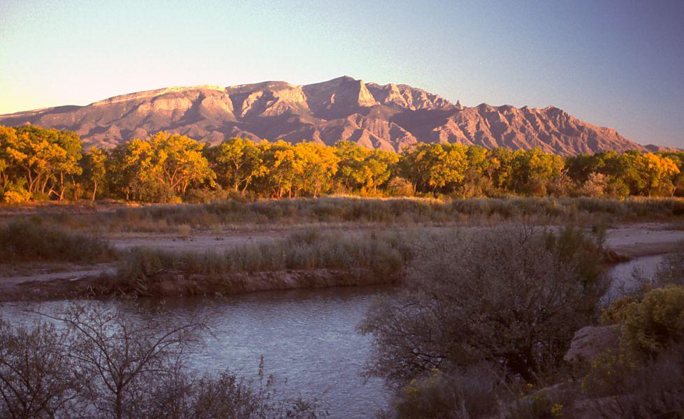 Sunlit mountain with trees by a river at sunset.