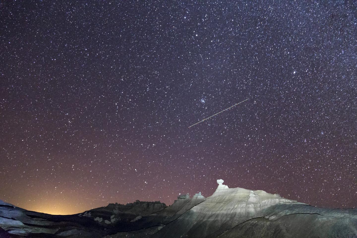 Starry night sky over rocky landscape, faint meteor streak.