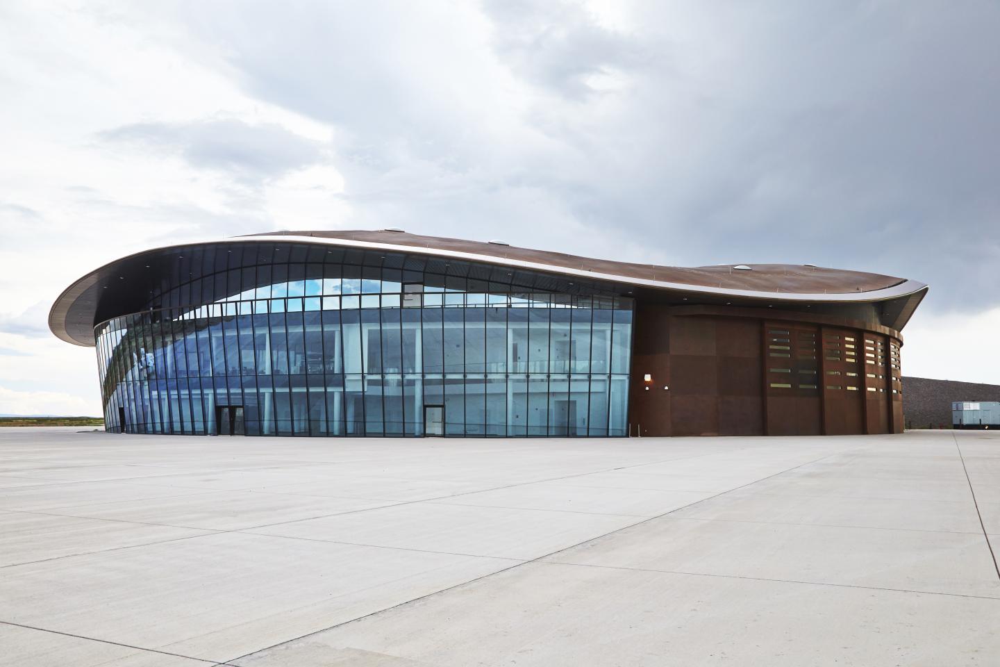 Space museum building with curved roof and glass facade under cloudy sky.