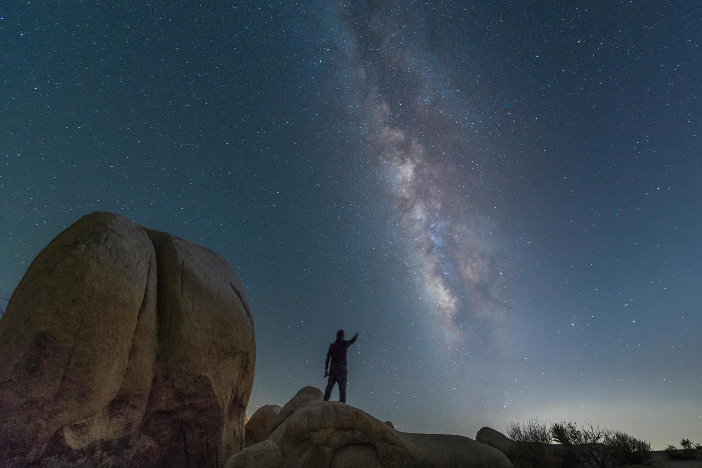 Person standing on rocks at Jumbo Rocks Campground, pointing at starry sky with Milky Way.