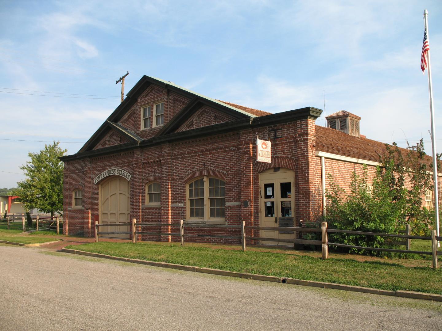 Historic red brick firehouse with a flagpole, wooden fence, and clear sky.