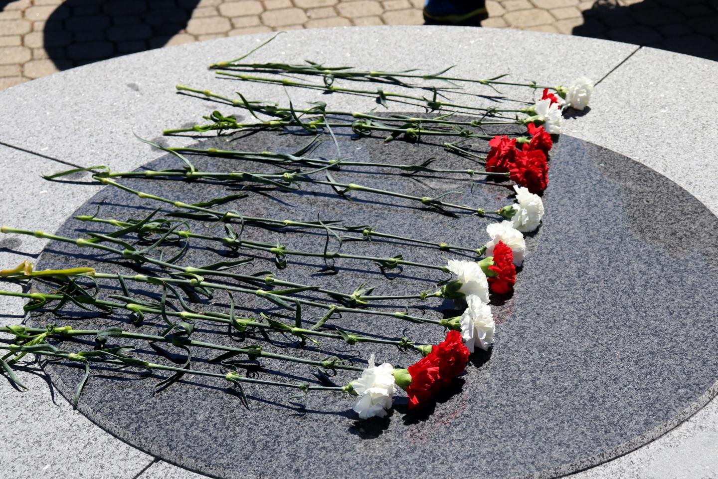 Red and white flowers laid on a stone memorial.