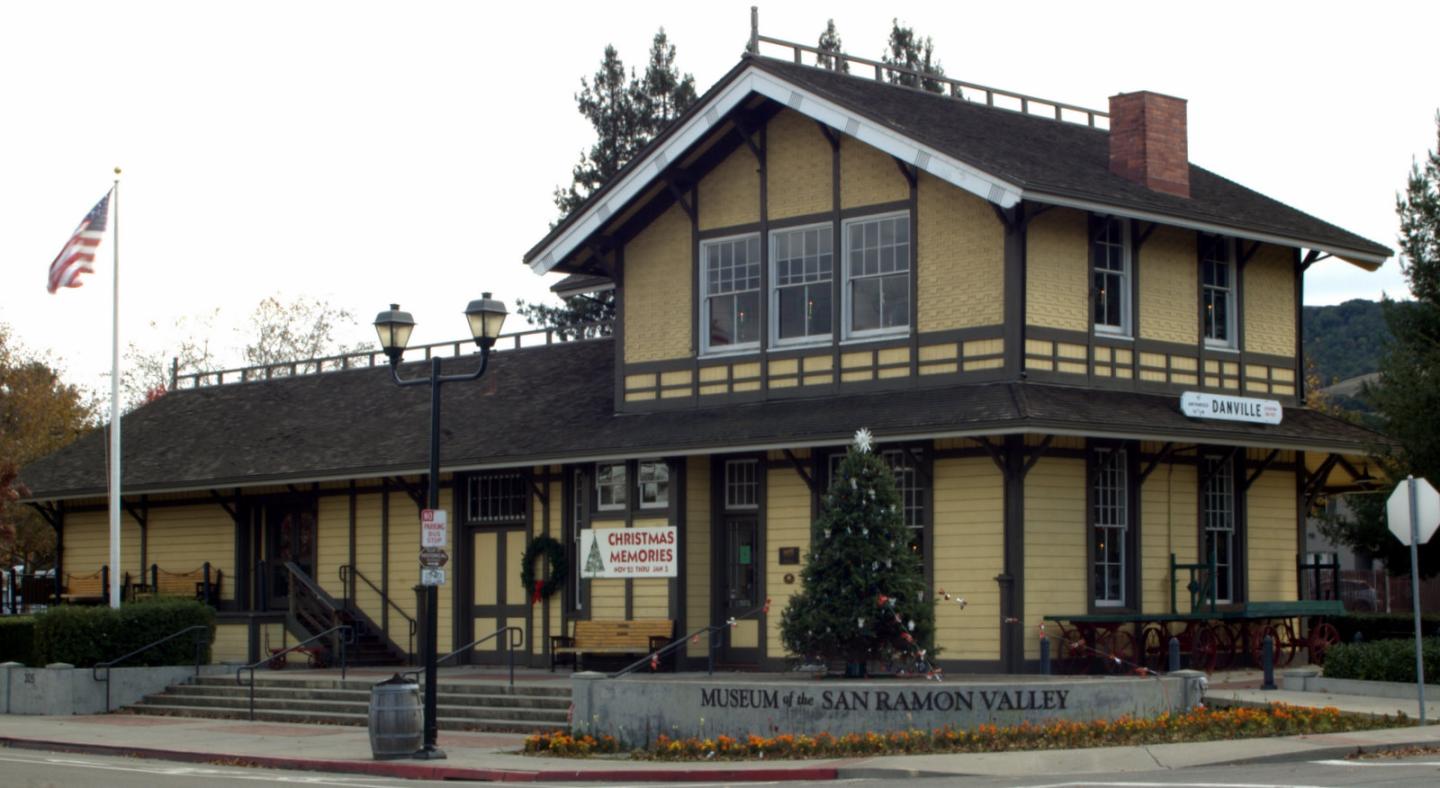 Museum of the San Ramon Valley with holiday decorations and a U.S. flag, surrounded by trees.