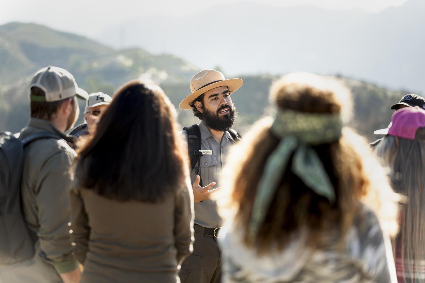 Park ranger talking to a group outdoors with mountains in the background.