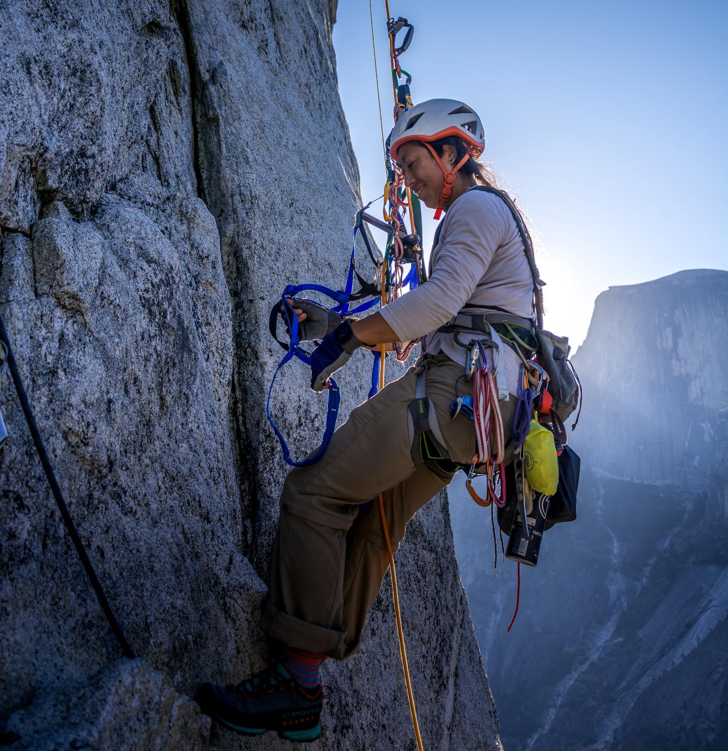 Rock climber ascending a steep cliff face with climbing gear.