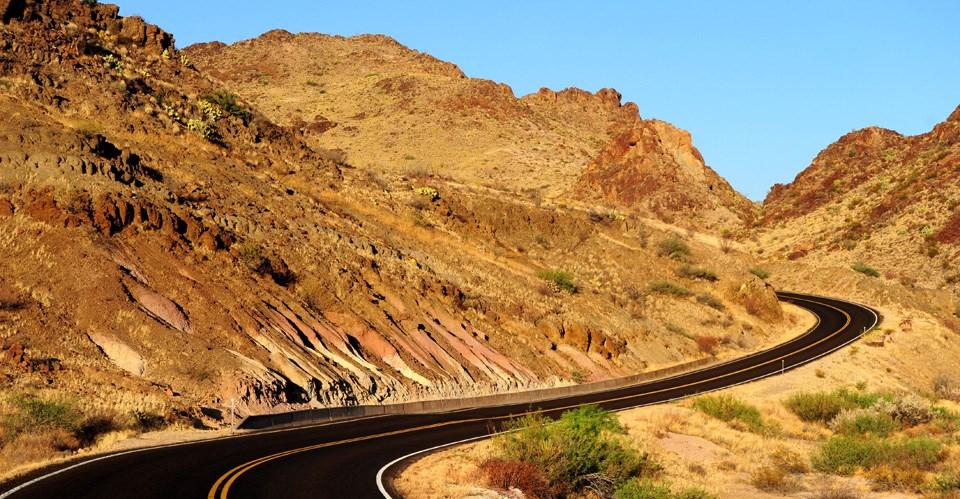 Winding desert road among rocky hills under a clear blue sky.