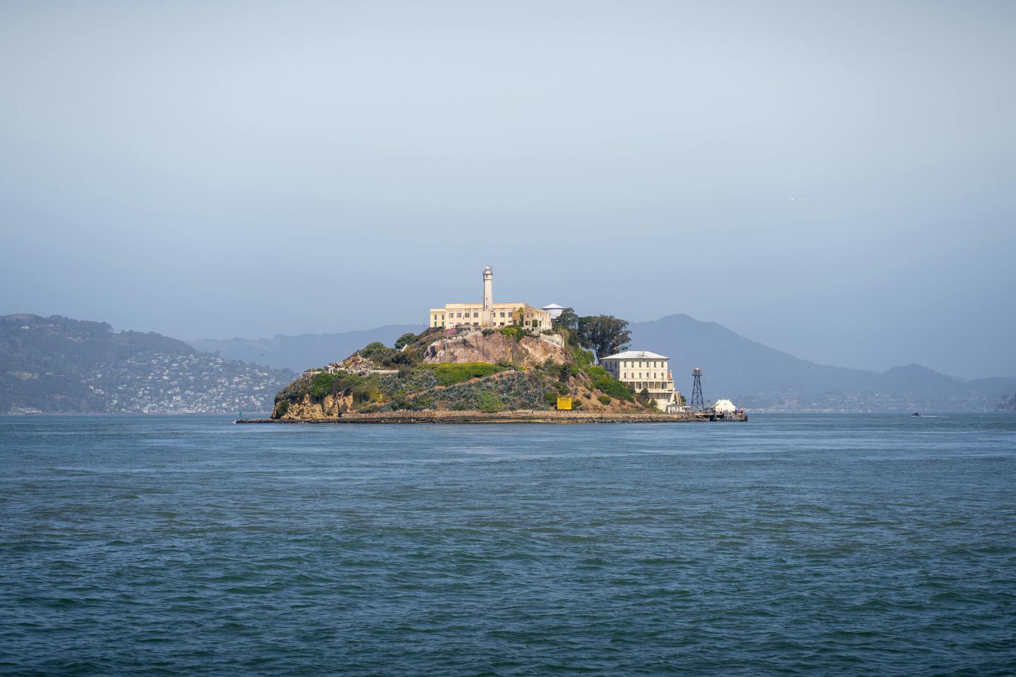 Alcatraz Island surrounded by blue water and distant hills.